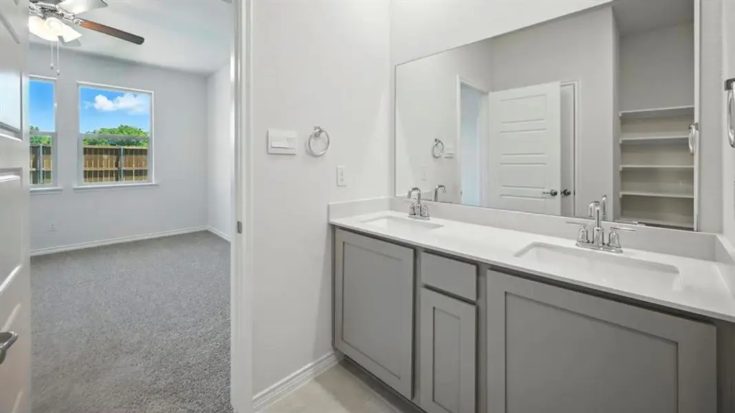 Full bathroom featuring double vanity, light colored carpet, a ceiling fan, and a spacious closet