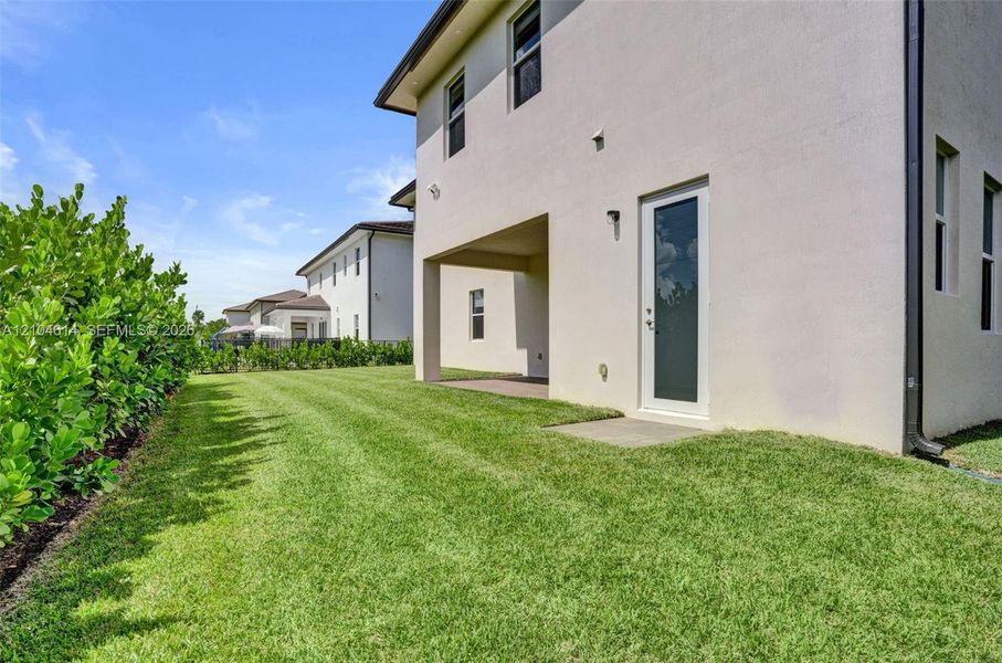 Expansive exterior with light-toned stucco, multiple windows, covered patio, and a privacy hedge