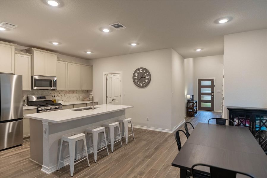 Kitchen with appliances with stainless steel finishes, a breakfast bar, wood tiled floors, decorative backsplash, and recessed lighting Kitchen with appliances with stainless steel finishes, a breakfast bar, wood tiled floors, decorative backsplash, and recessed lighting