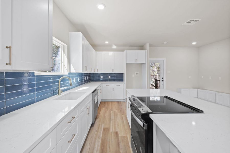 Kitchen featuring black / electric stove, light stone countertops, white cabinetry, light wood-style floors, and recessed lighting Kitchen featuring black / electric stove, light stone countertops, white cabinetry, light wood-style floors, and recessed lighting