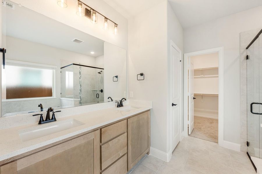Master bathroom with double vanity, quartz countertops, glass shower, and walk-in closet entrance