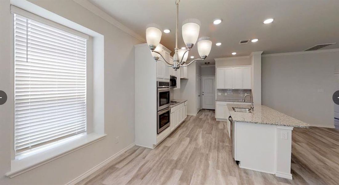 Kitchen featuring a sink, ornamental molding, backsplash, light wood-style floors, and white cabinetry