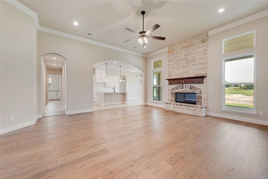 Unfurnished living room featuring crown molding, ceiling fan, arched walkways, light wood-type flooring, and a fireplace