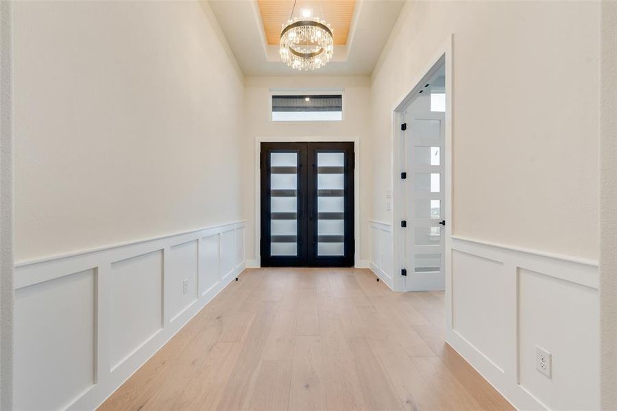 Foyer featuring a chandelier, a decorative wall, light wood-style floors, a wainscoted wall, and a tray ceiling Foyer featuring a chandelier, a decorative wall, light wood-style floors, a wainscoted wall, and a tray ceiling