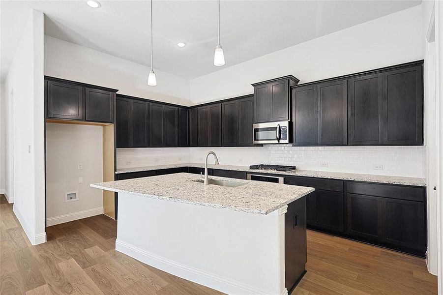 Kitchen with sink, stainless steel appliances, light stone counters, an island with sink, and light wood-type flooring