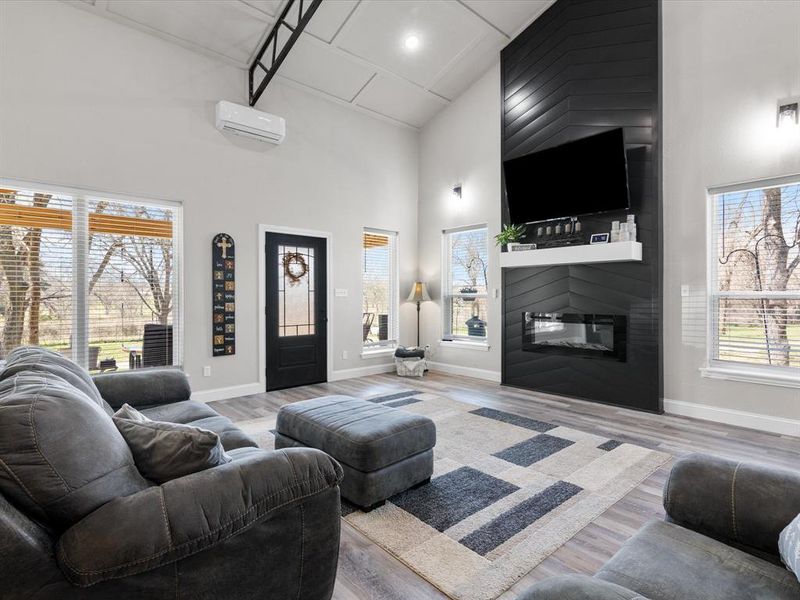 Living area featuring a high ceiling, an AC wall unit, wood finished floors, and a fireplace