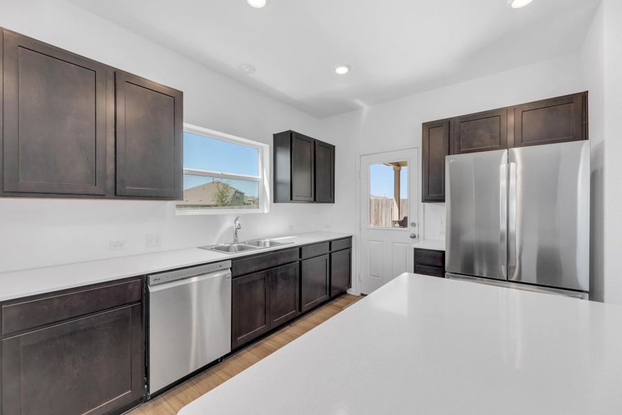 Kitchen with stainless steel appliances, light countertops, a sink, and dark brown cabinets