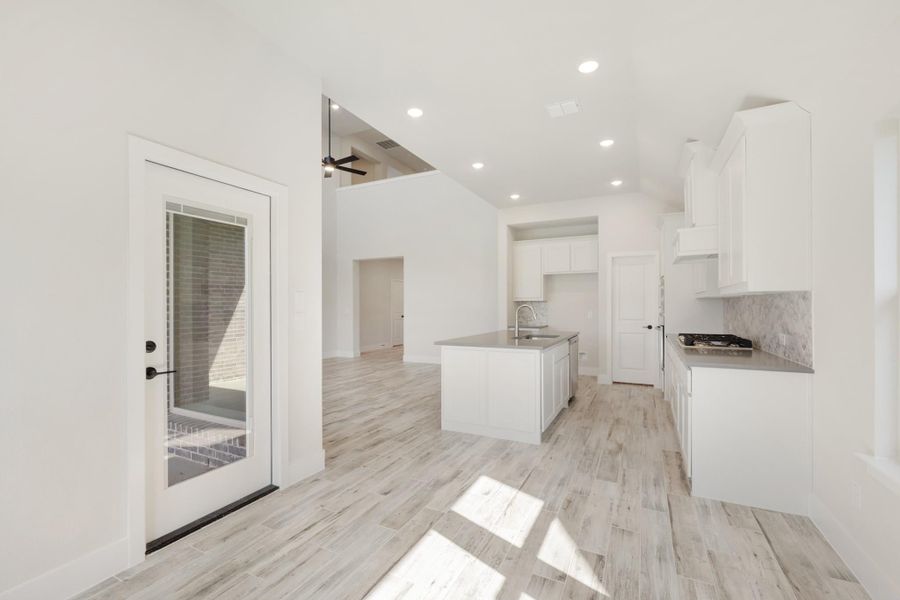 Open kitchen with white cabinets, center island, gray countertops, tile backsplash, and light wood-look floors Open kitchen with white cabinets, center island, gray countertops, tile backsplash, and light wood-look floors