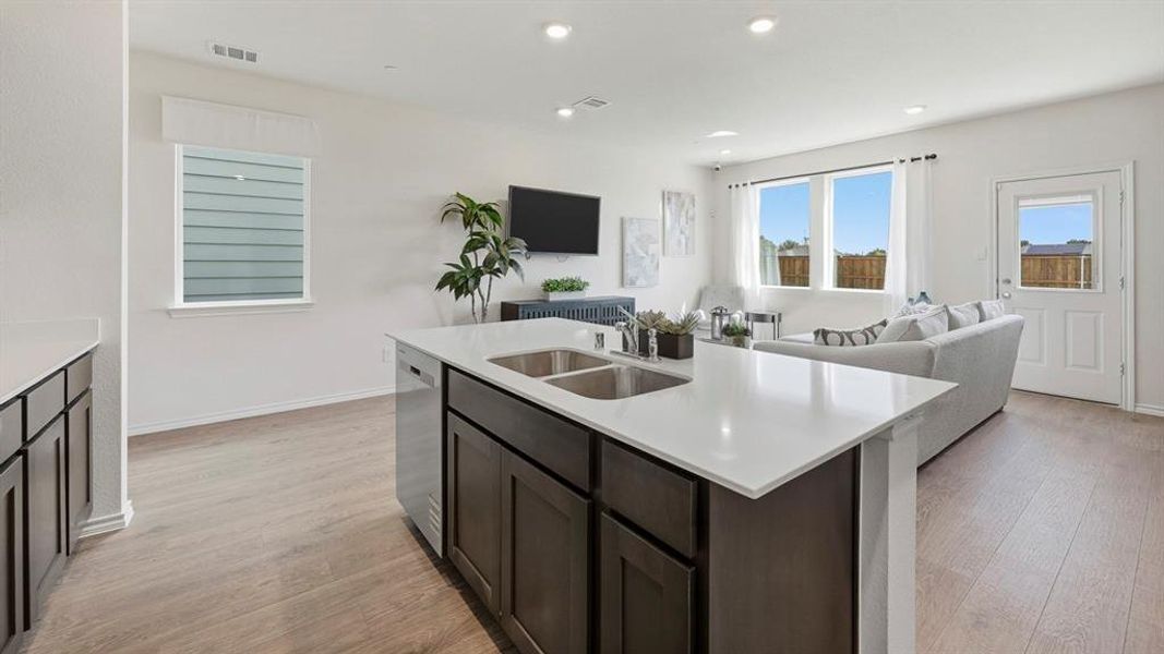 Kitchen featuring open floor plan, light wood-style floors, a center island with sink, dark brown cabinetry, and dishwasher Kitchen featuring open floor plan, light wood-style floors, a center island with sink, dark brown cabinetry, and dishwasher