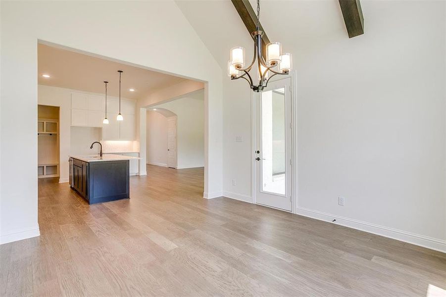 Unfurnished living room with high vaulted ceiling, light wood-type flooring, a notable chandelier, and beam ceiling