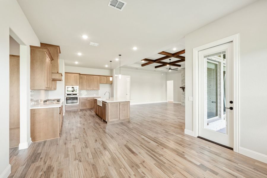 Open-concept kitchen with wood cabinets, center island, and coffered ceiling, flowing into living area with hardwood floors. Open-concept kitchen with wood cabinets, center island, and coffered ceiling, flowing into living area with hardwood floors.