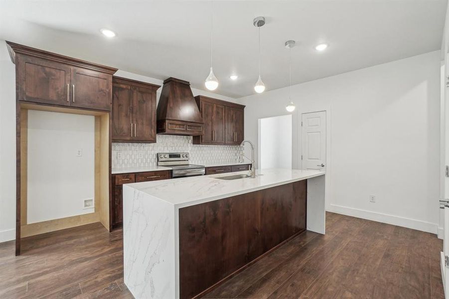 Kitchen with sink, hanging light fixtures, premium range hood, stainless steel range with electric stovetop, and dark brown cabinets