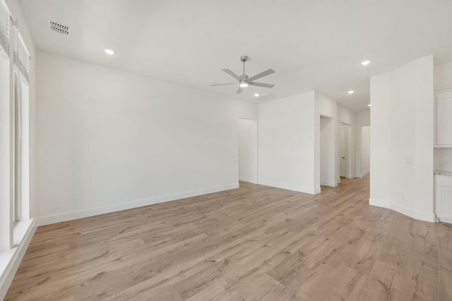 Empty living room with light wood floors, white walls, and ceiling fan with recessed lighting Empty living room with light wood floors, white walls, and ceiling fan with recessed lighting