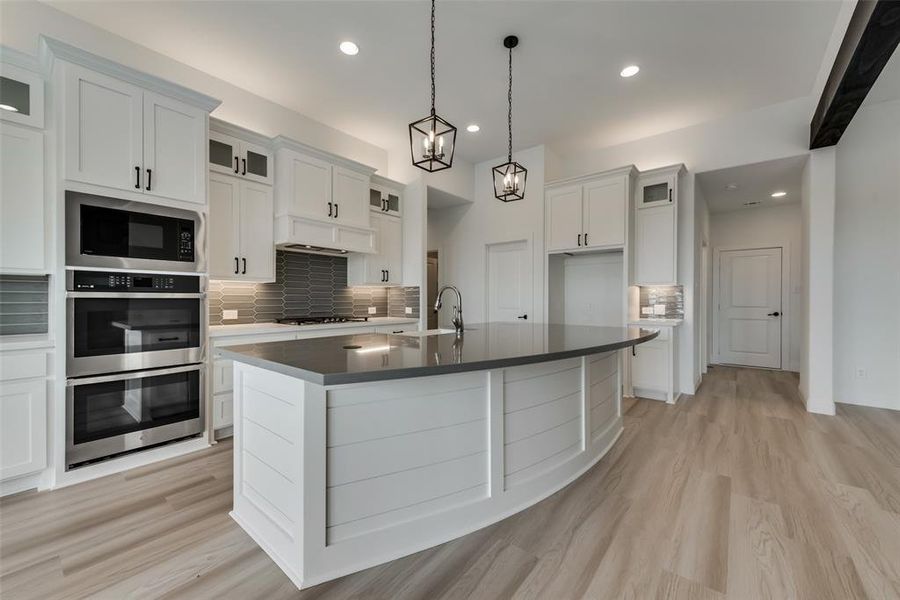 Kitchen with an island with sink, white cabinets, tasteful backsplash, and stainless steel appliances