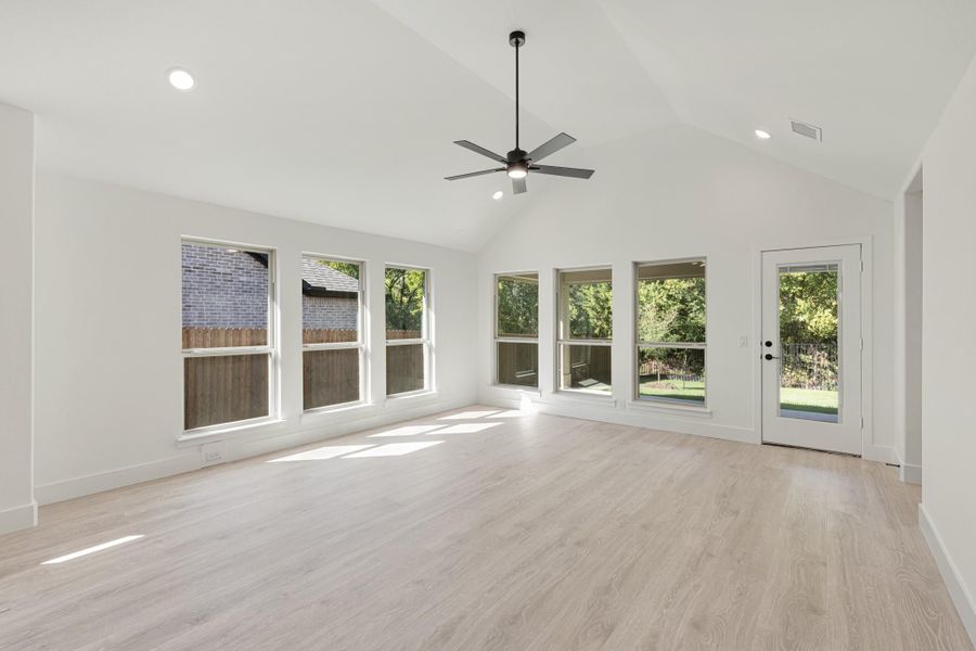 Open living area with vaulted ceiling, ceiling fan, light wood floors, and large windows overlooking backyard