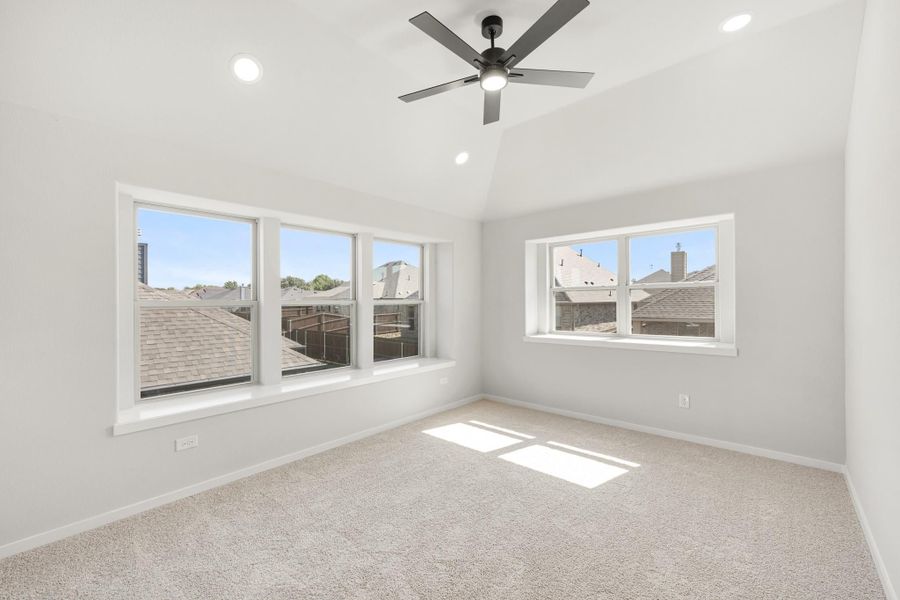 Empty bedroom with vaulted ceiling, ceiling fan, carpet flooring, and large windows with neighborhood views Empty bedroom with vaulted ceiling, ceiling fan, carpet flooring, and large windows with neighborhood views