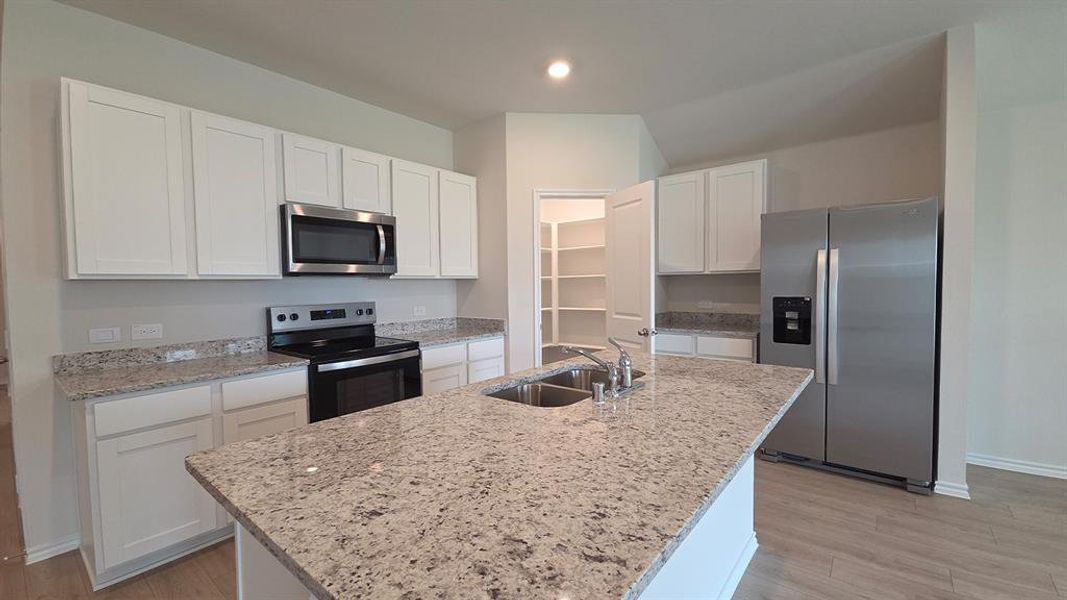 Kitchen featuring an island with a double basin sink, white cabinetry, granite countertops, stainless steel appliances, and a pantry with shelving