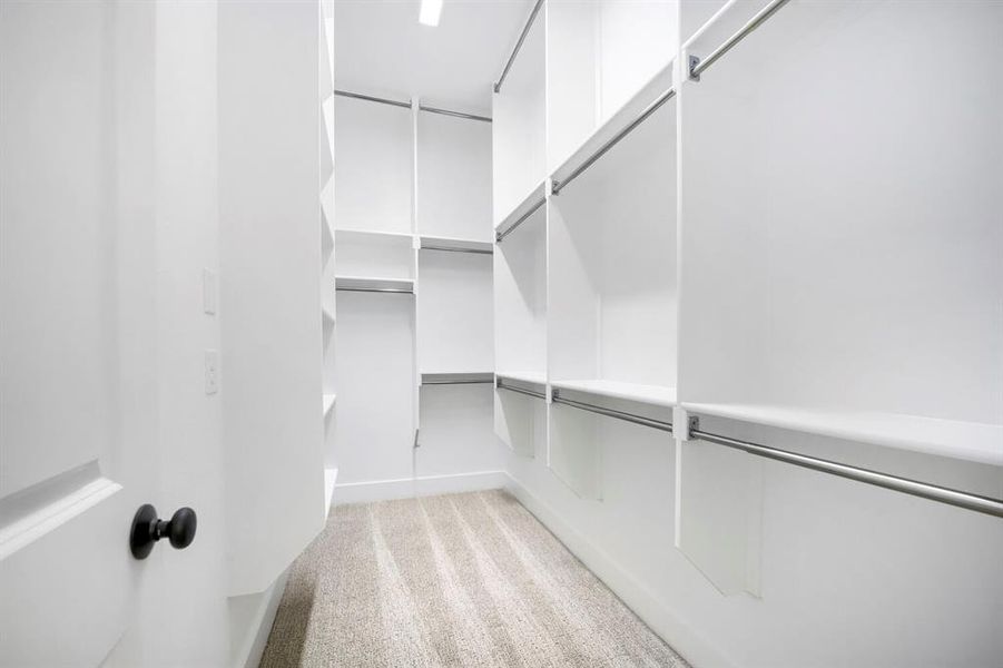 Walk-in closet featuring built-in white shelving, multiple hanging rods, recessed lighting, and light-toned carpeting Walk-in closet featuring built-in white shelving, multiple hanging rods, recessed lighting, and light-toned carpeting