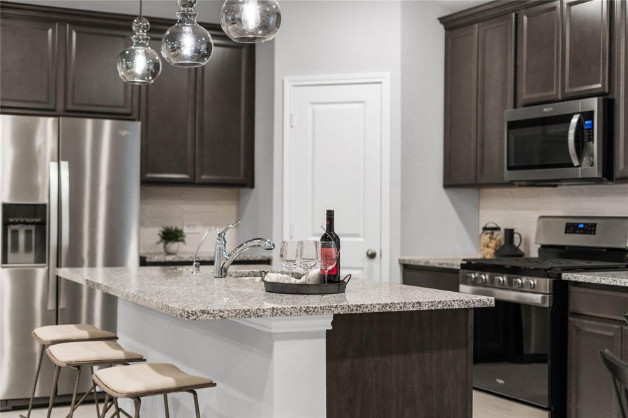 The heart of the home is this beautifully designed kitchen, featuring dark shaker-style cabinetry, sleek granite countertops, and a full suite of stainless steel appliances. A large central island with an integrated breakfast bar provides ample prep and dining space, illuminated by modern pendant and recessed lighting.