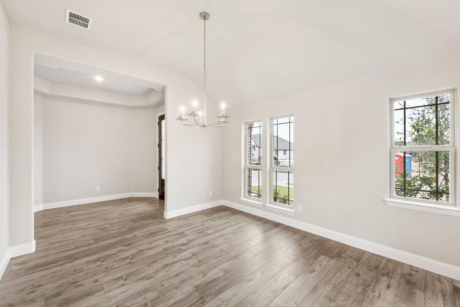 Empty dining room with chandelier, hardwood floors, and large windows overlooking neighborhood
