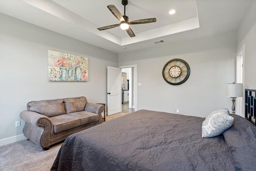 Bedroom featuring ceiling fan, light colored carpet, and a tray ceiling