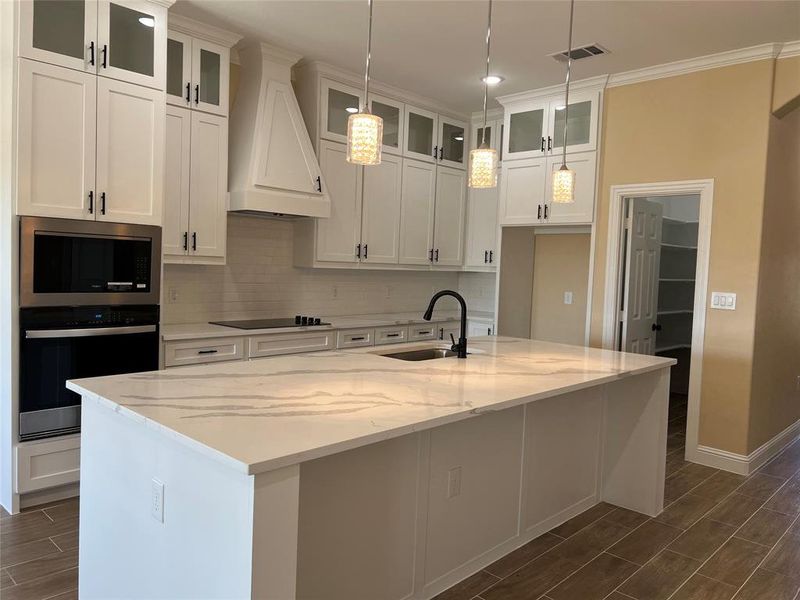 Kitchen featuring a large central island with a stone countertop, white shaker cabinetry, stainless steel built-in appliances, and a tile backsplash