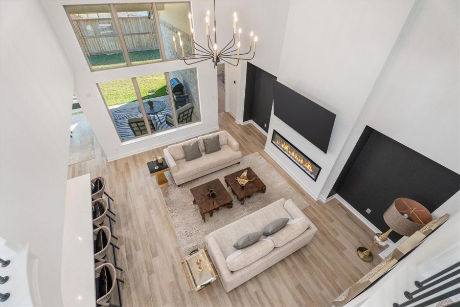 This spacious living area features high ceilings, a modern chandelier, and a sleek fireplace. Large windows offer plenty of natural light, while an open layout connects to a cozy outdoor patio. Ideal for entertaining, the room is elegantly furnished with neutral tones and stylish accents.