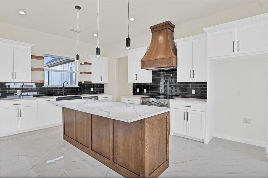 Kitchen featuring custom exhaust hood, light stone counters, decorative light fixtures, a center island, and white cabinets