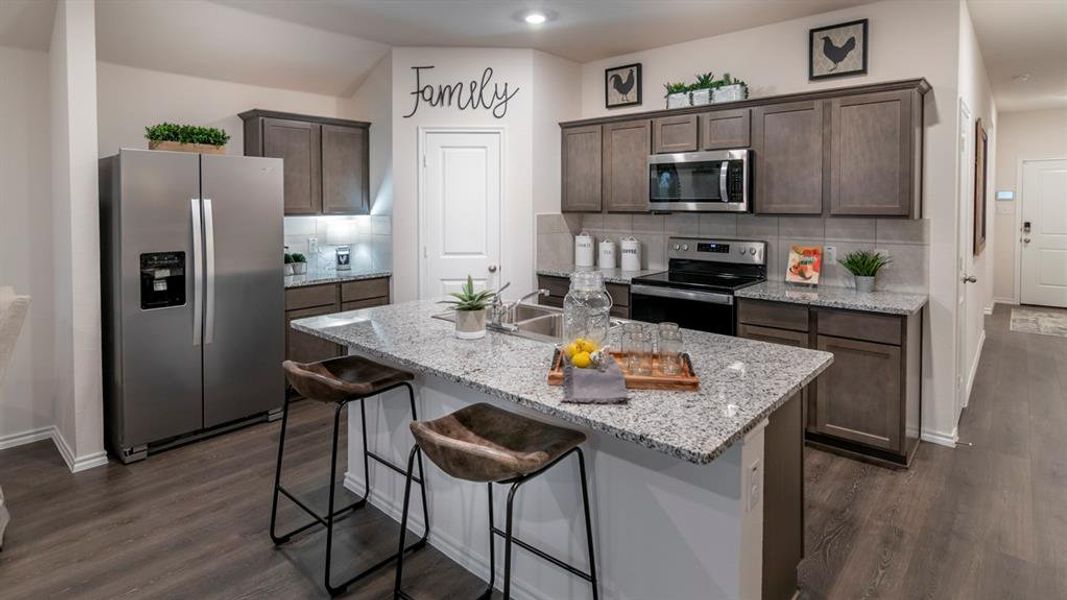 Kitchen featuring decorative backsplash, stainless steel appliances, dark wood finish cabinetry, and a kitchen bar