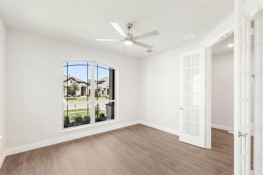 Empty room with hardwood floors, ceiling fan, arched window, and French doors