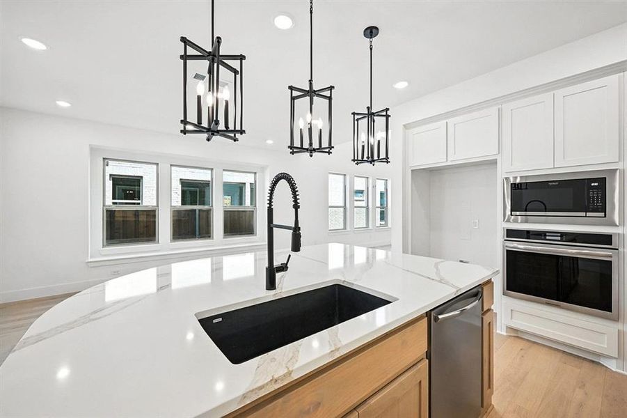 Kitchen with light wood-style floors, stainless steel appliances, hanging light fixtures, light stone countertops, and white cabinetry Kitchen with light wood-style floors, stainless steel appliances, hanging light fixtures, light stone countertops, and white cabinetry