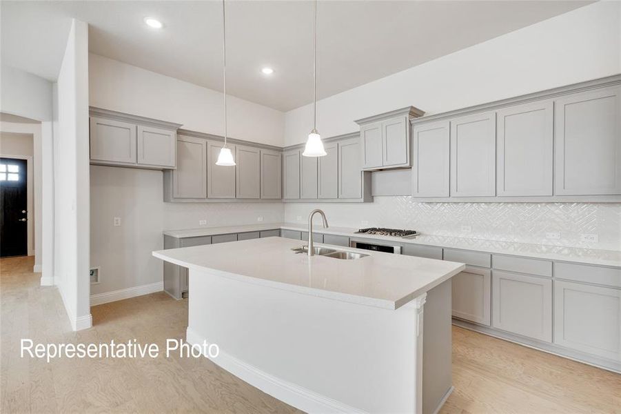 Kitchen with hanging light fixtures, light hardwood / wood-style floors, tasteful backsplash, a kitchen island with sink, and sink