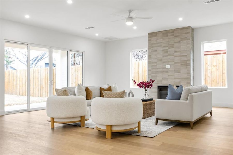 Living room featuring ceiling fan, light hardwood / wood-style flooring, a large fireplace, and a healthy amount of sunlight