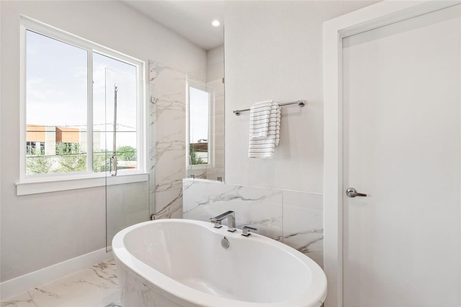 A sculptural soaking tub anchors the ensuite, framed by full-height tile and natural light for a calm, spa-forward finish.