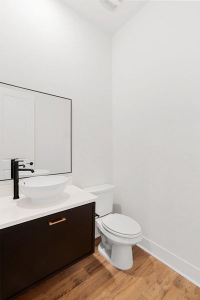 A stylish half bath features a modern vessel sink, sleek black faucet, and rich wood flooring.