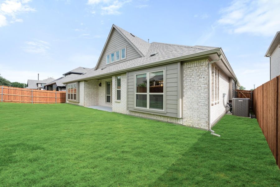 Rear exterior of two-story brick and siding home with large backyard, wood privacy fence, and AC unit Rear exterior of two-story brick and siding home with large backyard, wood privacy fence, and AC unit