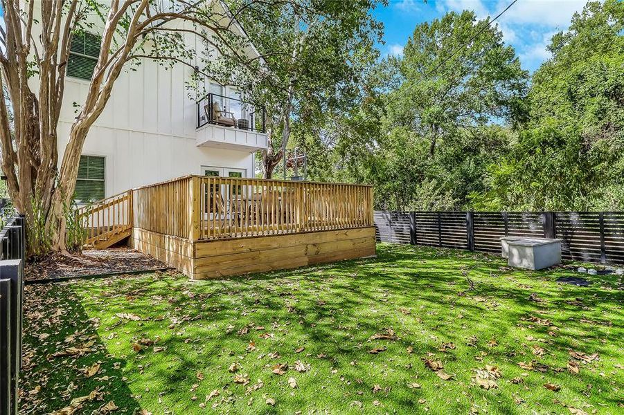 A spacious backyard features a raised wooden deck perfect for outdoor gatherings and a private balcony above.