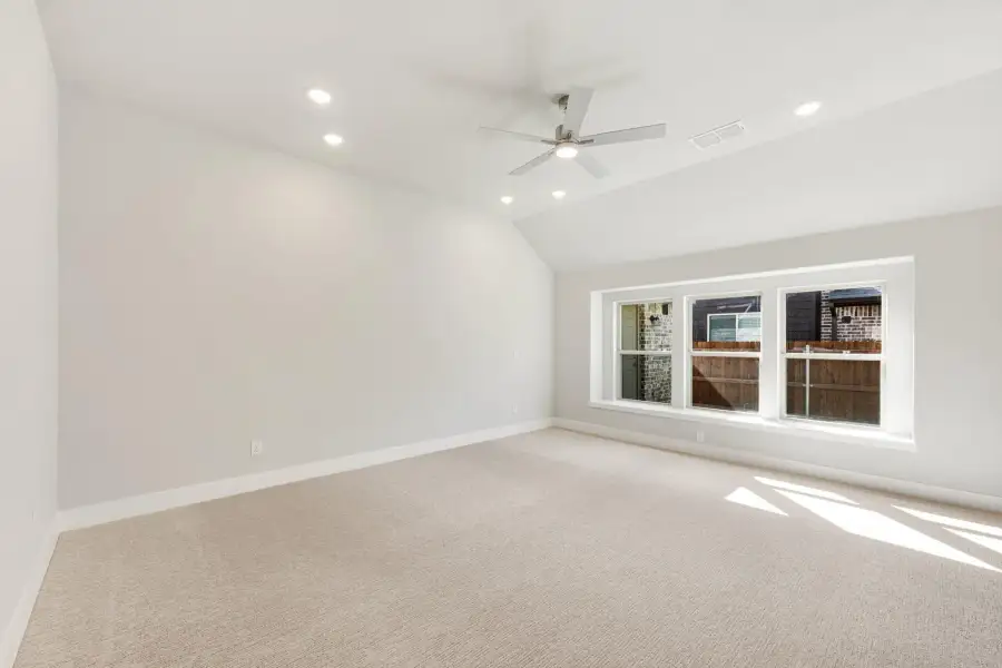 Empty bedroom with vaulted ceiling, ceiling fan, recessed lighting, and large windows with carpet flooring