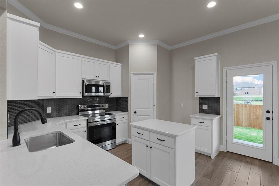 Kitchen with white cabinetry, stainless steel appliances, a center island, solid surface countertops, and wood-finish flooring