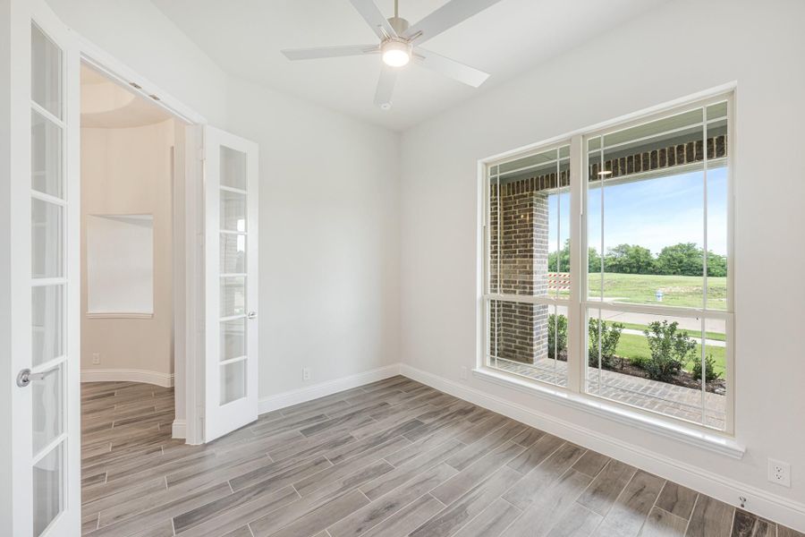 Empty room with wood-look tile floors, ceiling fan, large window, and French doors leading to adjacent space