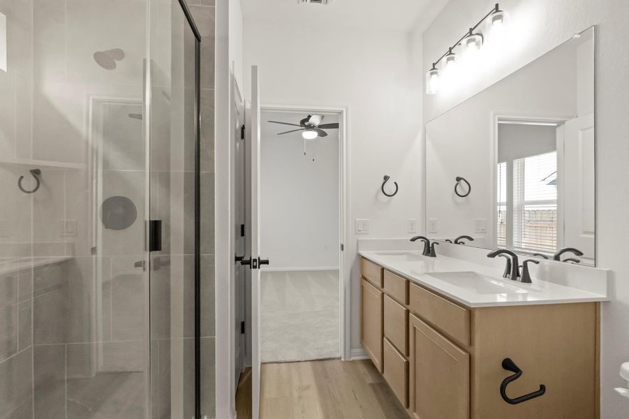 Full bathroom with double vanity, a shower stall, light wood-style floors, and a ceiling fan