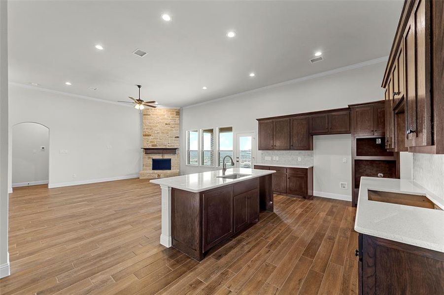 Kitchen with dark brown cabinetry, ceiling fan, sink, crown molding, and an island with sink