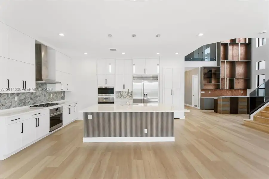 Kitchen featuring white cabinetry, wood-finish flooring, a central island with a solid-surface countertop, stainless steel appliances, and a decorative tile backsplash