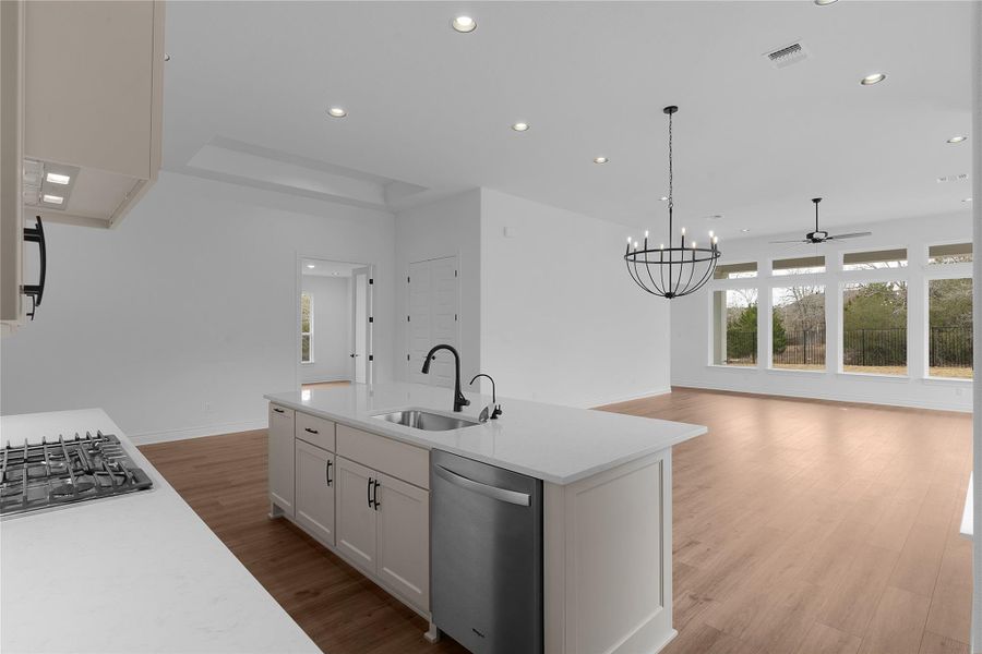 Kitchen featuring light wood-style flooring, stainless steel appliances, a chandelier, open floor plan, and light stone countertops