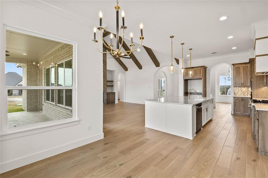 Expansive kitchen featuring a large central island, pendant lighting, wood-finish flooring, and built-in cabinetry