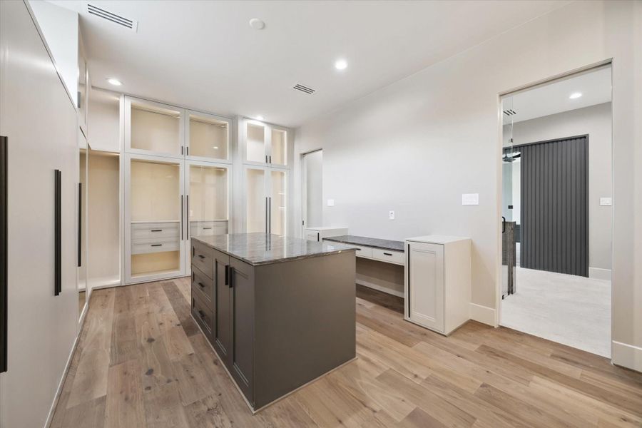 This expansive walk-in closet is thoughtfully designed with custom built-ins, featuring lighted glass-front cabinetry, abundant hanging space, and sleek storage drawers.