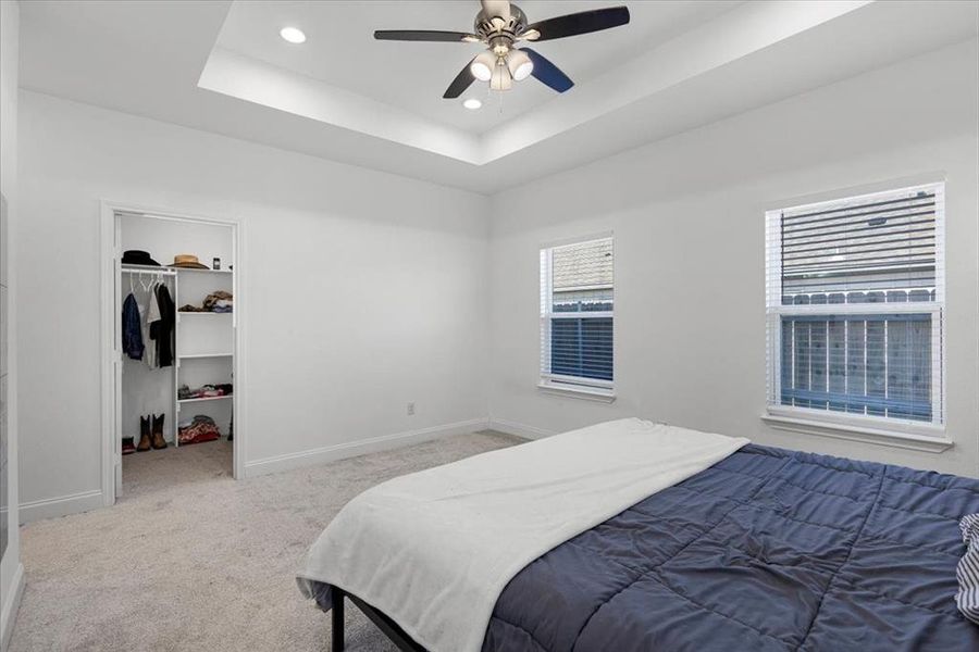 Carpeted bedroom with a spacious closet, a tray ceiling, recessed lighting, and a ceiling fan Carpeted bedroom with a spacious closet, a tray ceiling, recessed lighting, and a ceiling fan