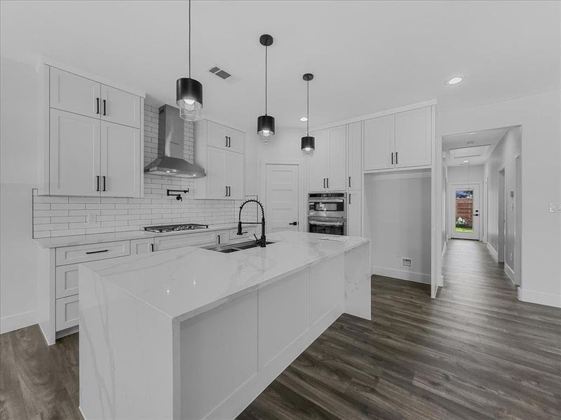 Kitchen featuring white cabinets, tasteful backsplash, light stone counters, a center island with sink, and hanging light fixtures Kitchen featuring white cabinets, tasteful backsplash, light stone counters, a center island with sink, and hanging light fixtures