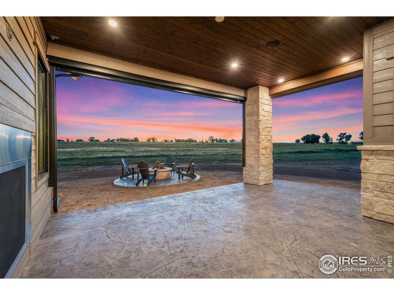 Back Covered Porch with Stamped Concrete, Two Sided Fireplace, Stubbed for Natural Gas Grill, Gas Firepit, and Remote Powered Sun Shade, Wired for Outdoor TV. Speakers Included