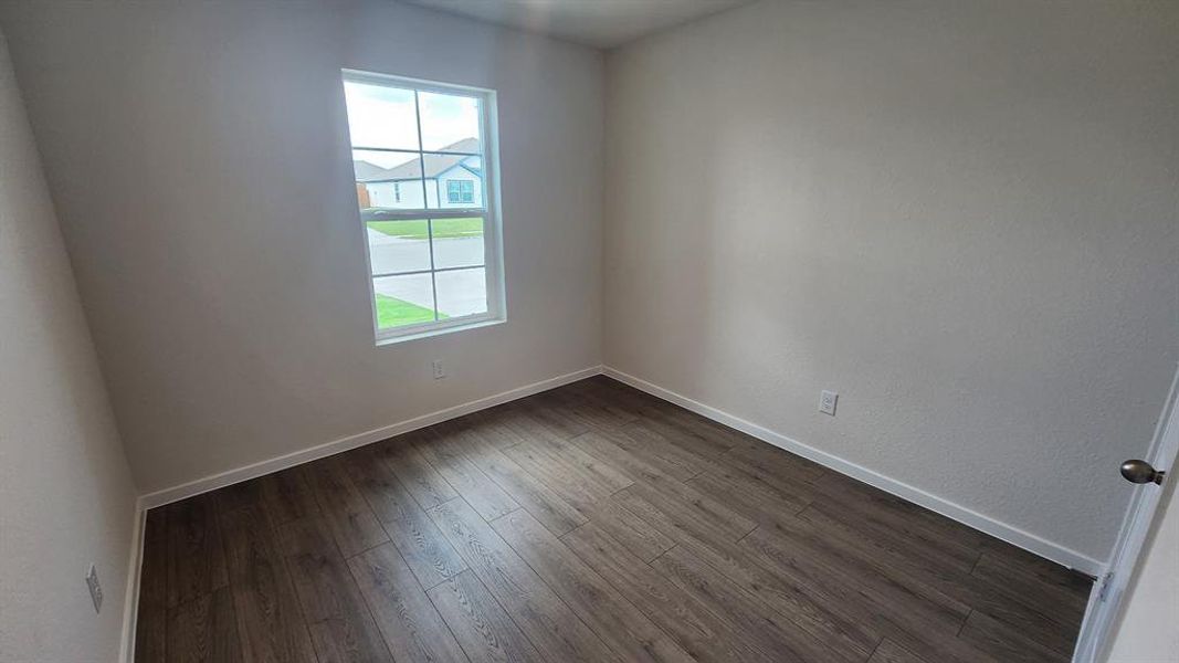 Room featuring wood-finish flooring, neutral wall tones, white baseboards, and a multi-pane window Room featuring wood-finish flooring, neutral wall tones, white baseboards, and a multi-pane window